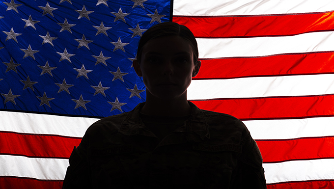 Senior Airman Zoe Wockenfuss stands in front of an illuminated American Flag
